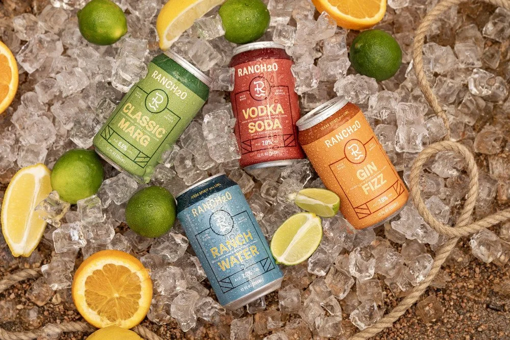  Four colorful Ranch20 canned cocktails arranged on ice with fresh oranges, lemons, and limes 