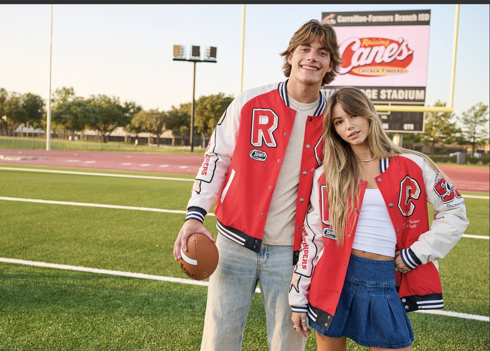  Young man and woman wearing red varsity jackets on a football field, with the man holding a football 