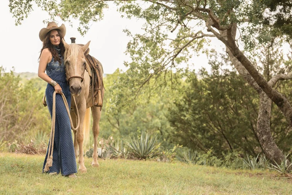 Woman in a cowboy hat standing beside a horse outdoors