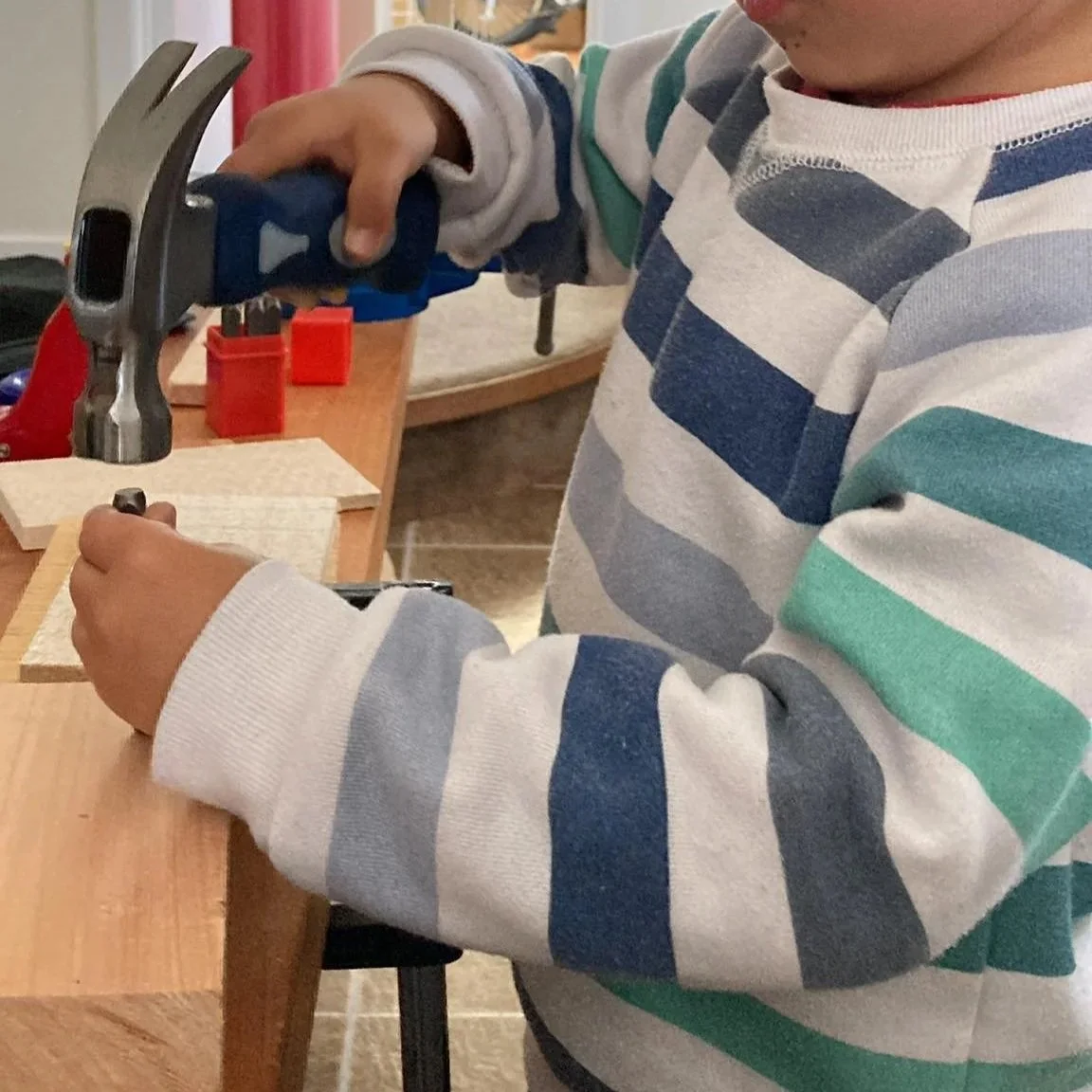 Young child stamping letters into wood with an alphabet punch during hands-on Technology learning