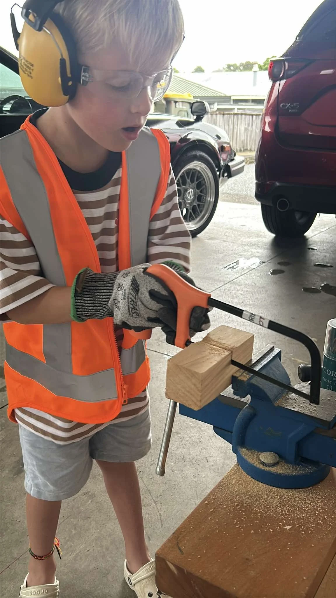 Child dressed as builder confidently sawing wood secured in a kids' bench vice – a safe and stable woodworking setup