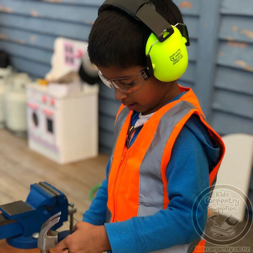 boy wearing child sized safety earmuffs and high visibility vest while doing carpentry
