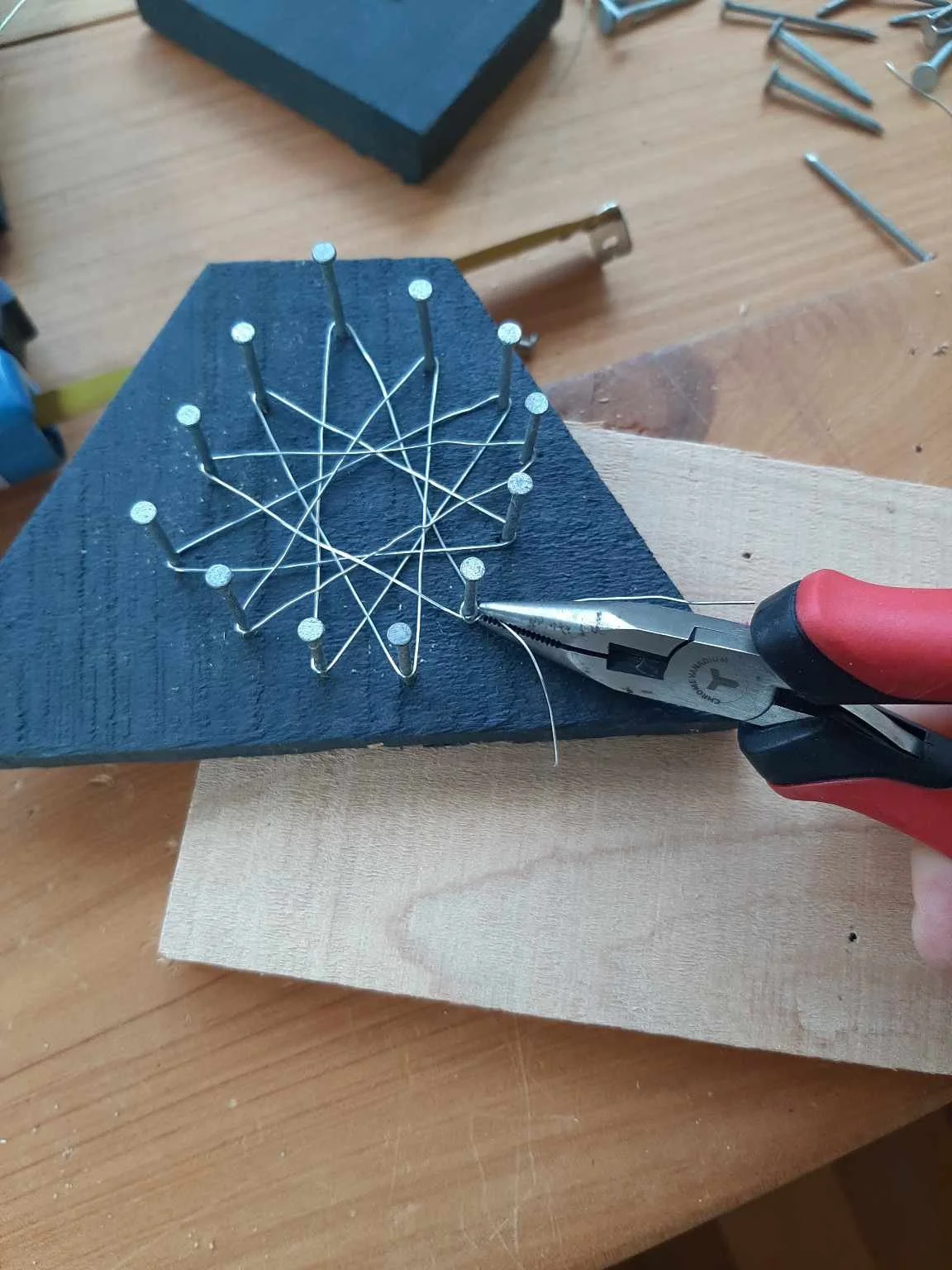 Small sprung craft pliers being used to twist wire to make a string art star