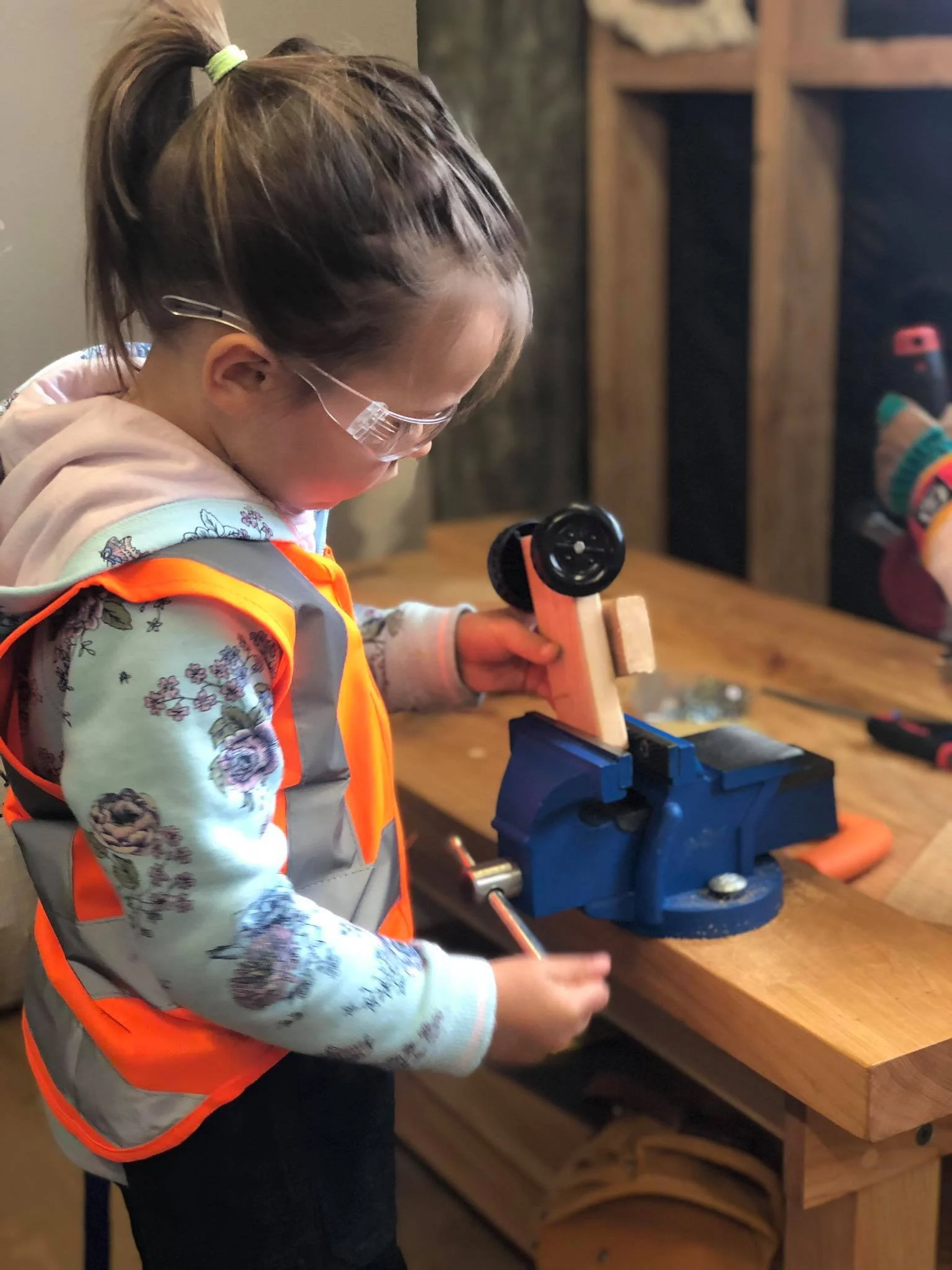 Young girl turning the handle of a kids' bench vice to securely clamp her woodwork project in place