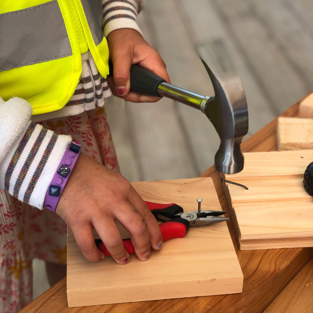 young girl using pliers to help hold nail and protect fingers while she learns to hammer.