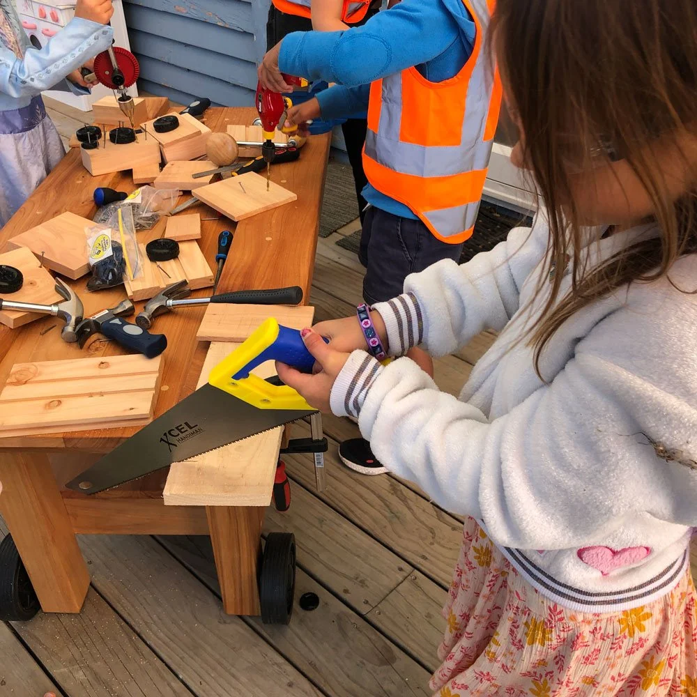 Child using a hand saw during a classroom woodworking activity with real kids carpentry tools