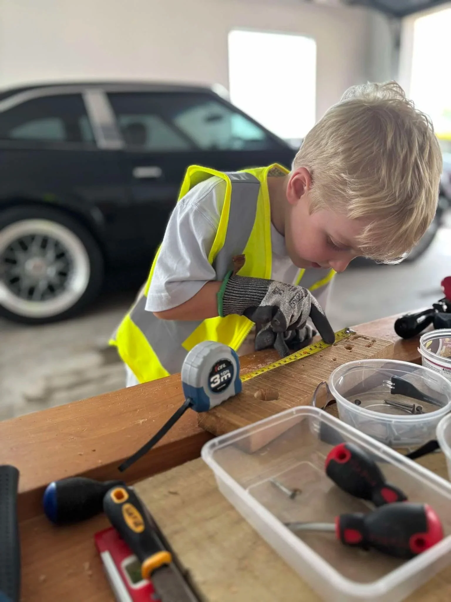 Child accurately measuring timber with a tape measure during a hands on carpentry project