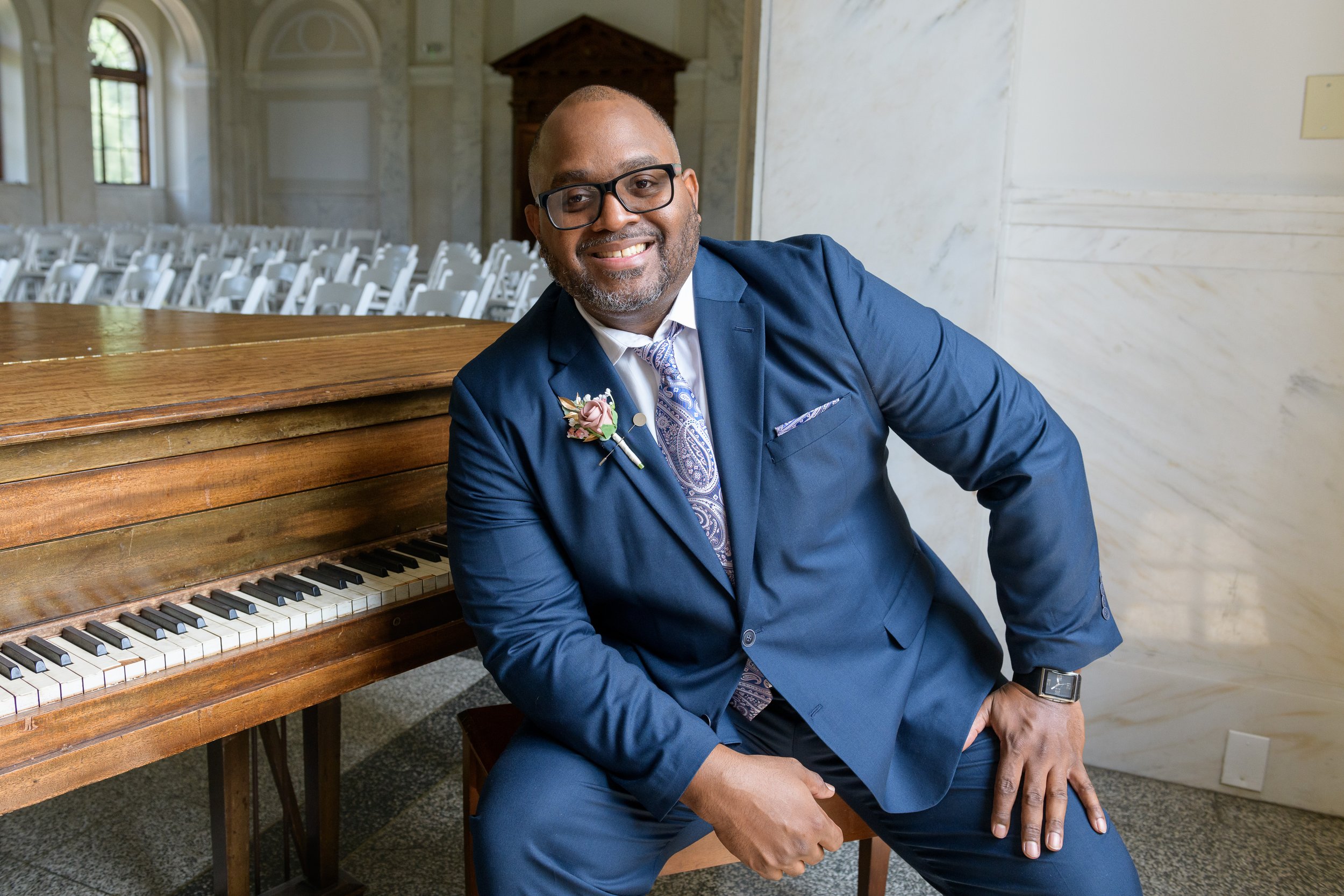 Groom smiles as he sits on piano bench of antique baby grand piano at this Dekalb Courthouse wedding in Decatur, GA