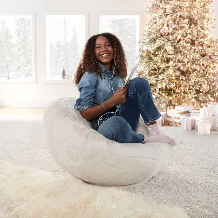  Girl sitting on a white bean bag chair in front of Christmas tree 