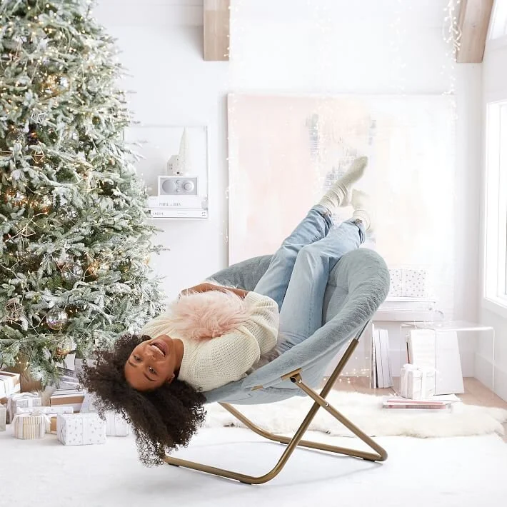  Girl laying upside down in a round chair in front of a Christmas tree 