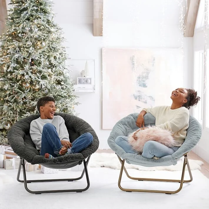  Boy and girl laughing on chairs in front of Christmas tree 