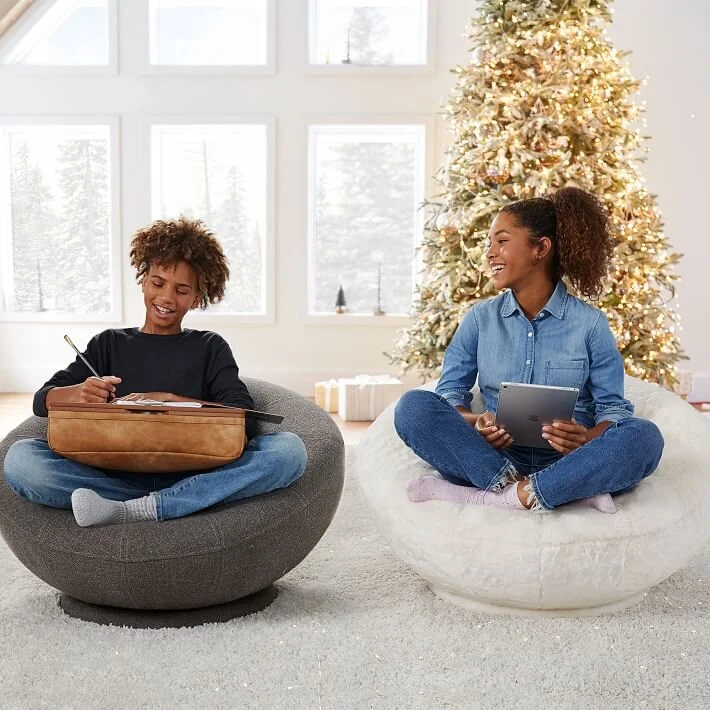  Boy and girl sitting on bean bag chairs in front of Christmas tree 