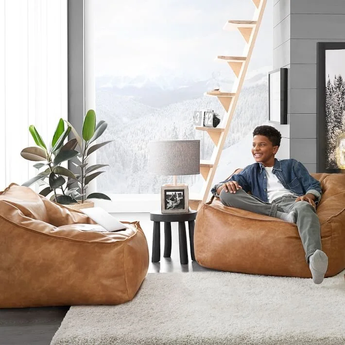  Boy sitting in a bright room on a brown bean bag chair 