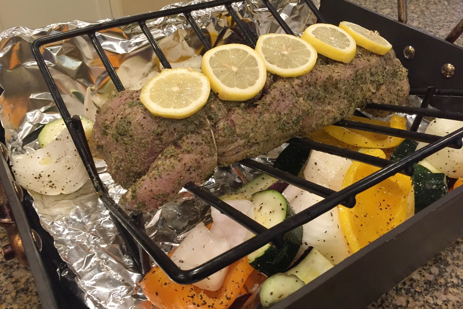 Tie the two halves together using butcher's (cotton) twine. Place on a rack within the roasting pan. Spread the vegetables around the pan after tossing them in olive oil, salt, and pepper. Place lemon slices over the tenderloin. Feel free to drizzle some lemon over the pork while you're at it.