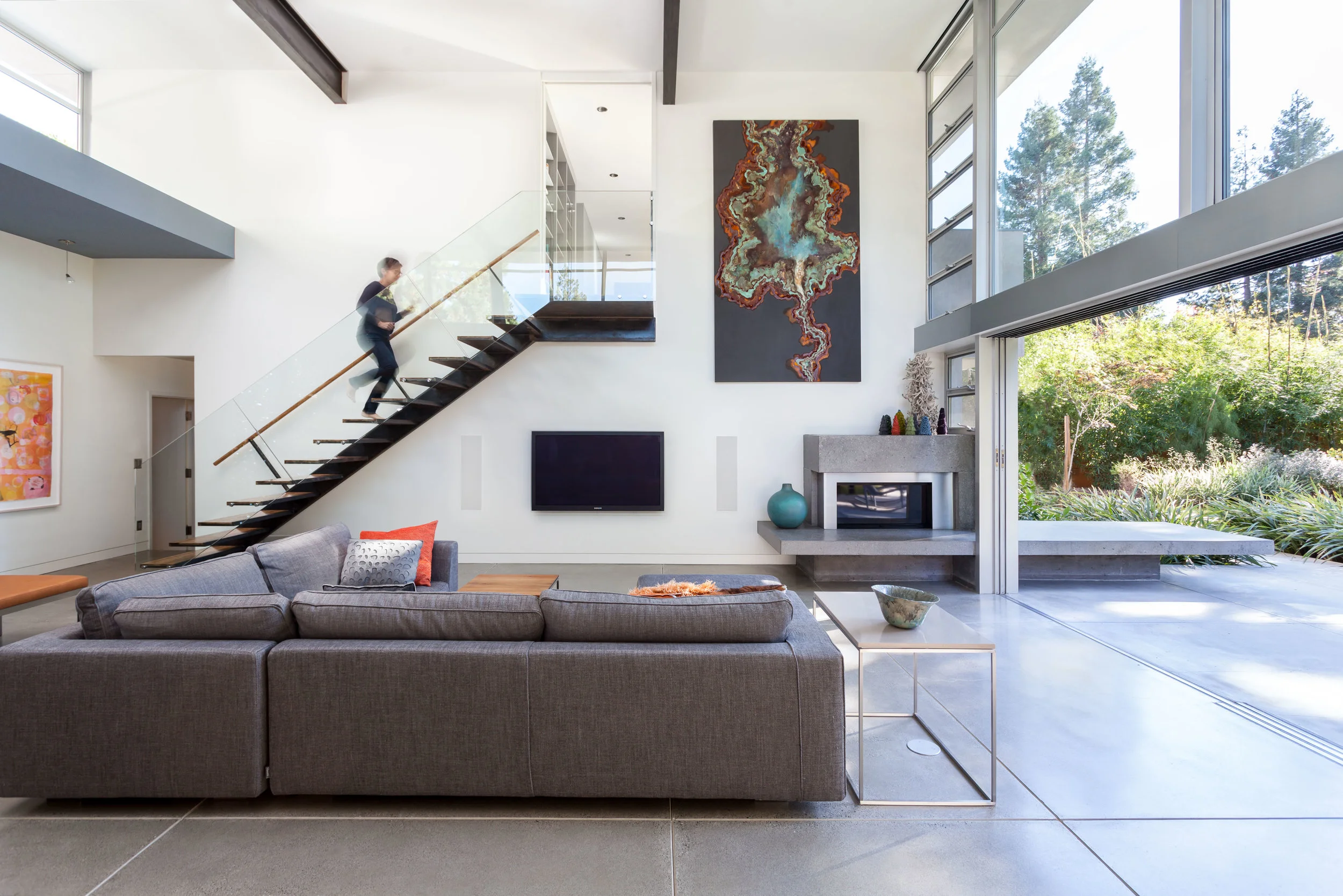 The fireplace hearth extends outside as a bench for the yard. The steel and glass stair balances the concrete.