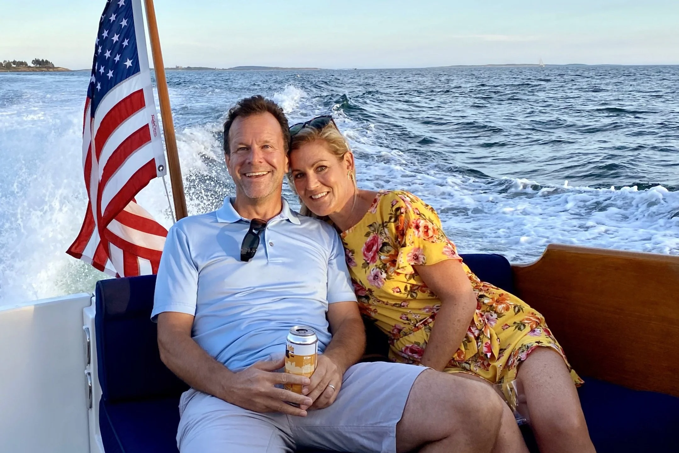Smiling couple on a boat with an American flag, ocean background.