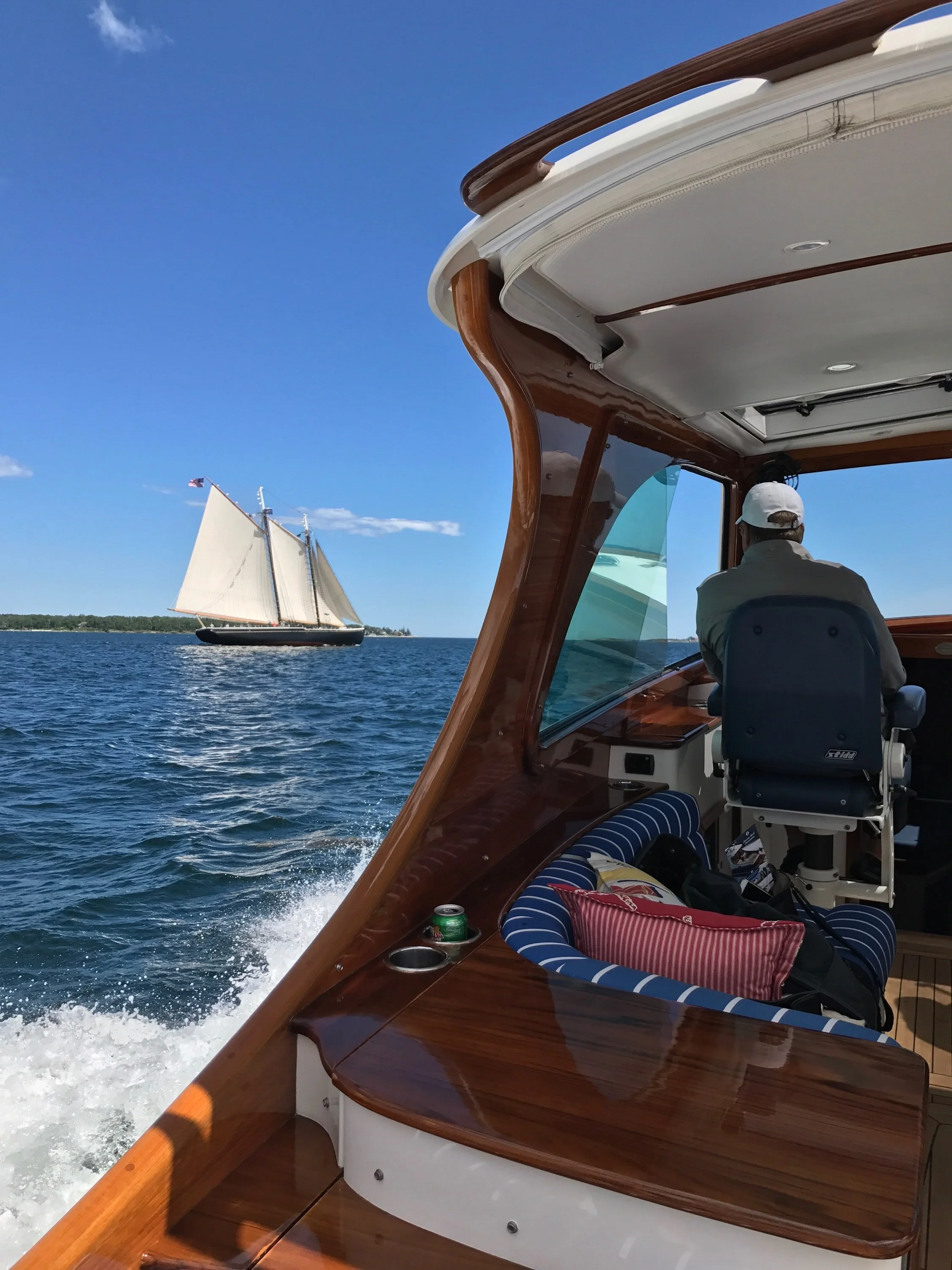 View from a motorboat interior on a sunny day, showing a sailboat with white sails on open water in the background.
