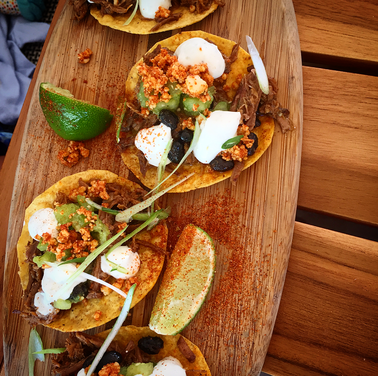 Beef Tostados topped with spiced queso, black bean puree, salsa verde, lime crema and cilantro