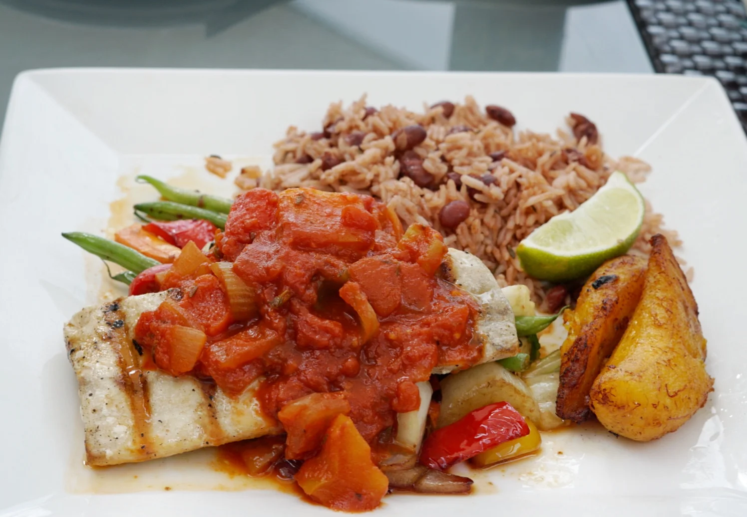 Cayman Style Mahi topped with a tomato-based sauce and served with green beans, sweet fried plantains and rice & beans