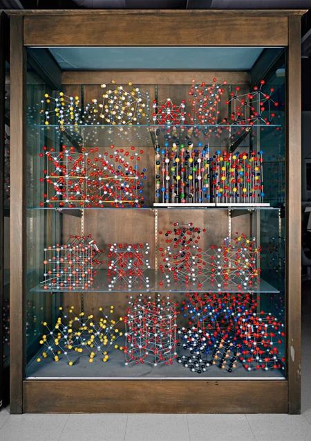 A display case showing various ball-and-stick models; the different colors represent different elements. Most are common minerals and were manufactured by the Leybold company for teaching purposes. On the left side of the third shelf down can be see…