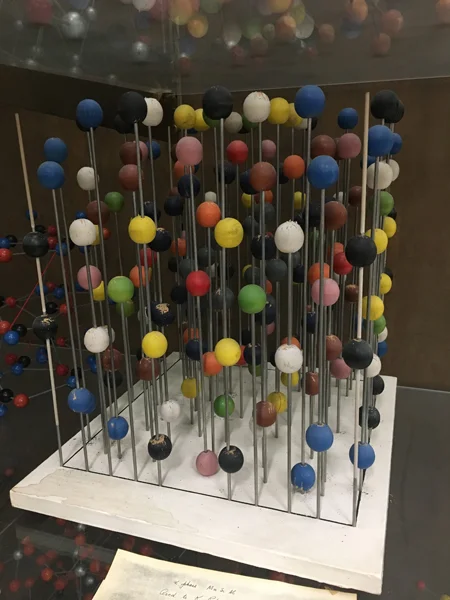 A model of the α phase of MnSiAl (Manganese Silicon Aluminum), an intermetallic compound. The vertical rods are merely to hold the atoms. The structure is cubic so that all three cell edges are equal and all angles are 90˚. The colors of the balls r…