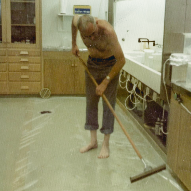 Color archival photograph of Caltech geochemist Clair C. Patterson mopping the floor of his laboratory as part of efforts to eliminate trace lead contamination from his research environment.