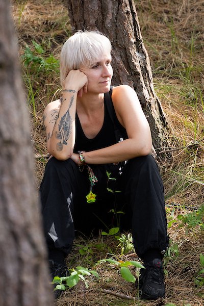 Maxi Meissner during Oerol 2026, freelancing for Company Marte Boneschansker, sitting outdoors among trees and grass, resting her head on her hand, wearing a black sleeveless top and black pants.