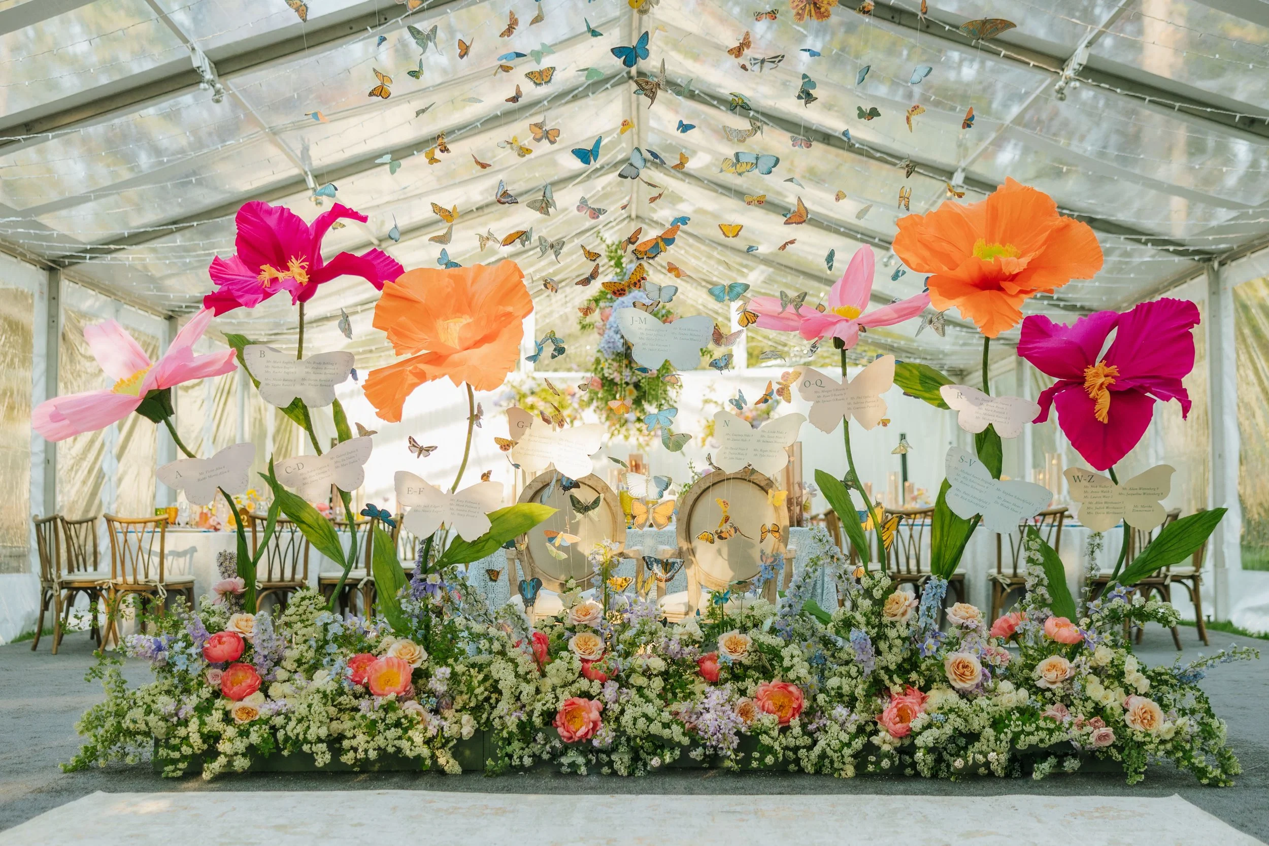 Lots of paper butterflies soaring up and out of real flowers and oversized paper flowers. Colorful and whimsical seating chart installation.