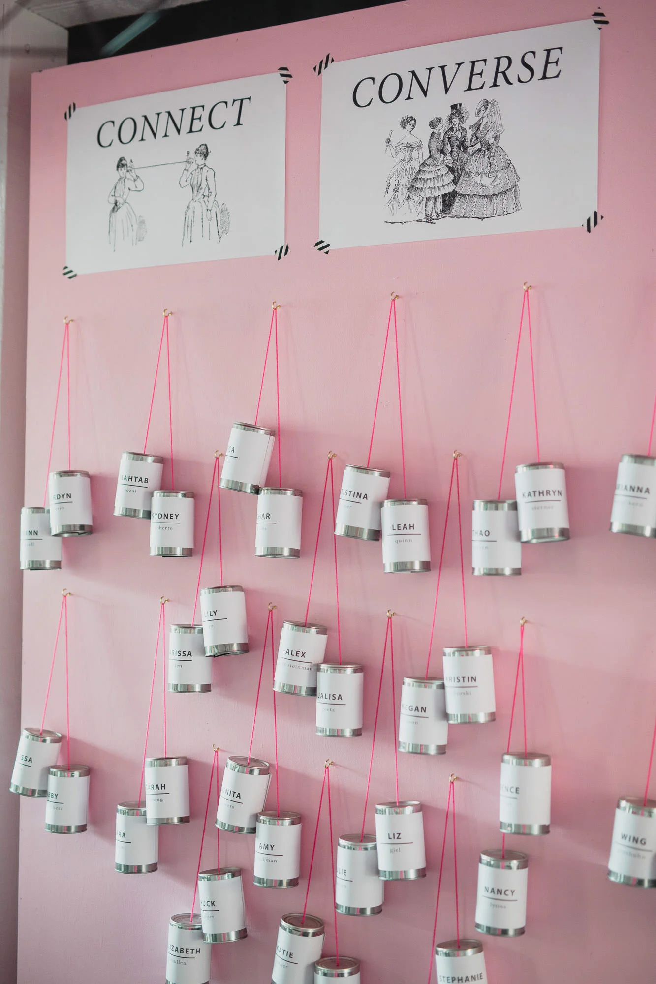  tin can telephones hang from pink string on pink wall 