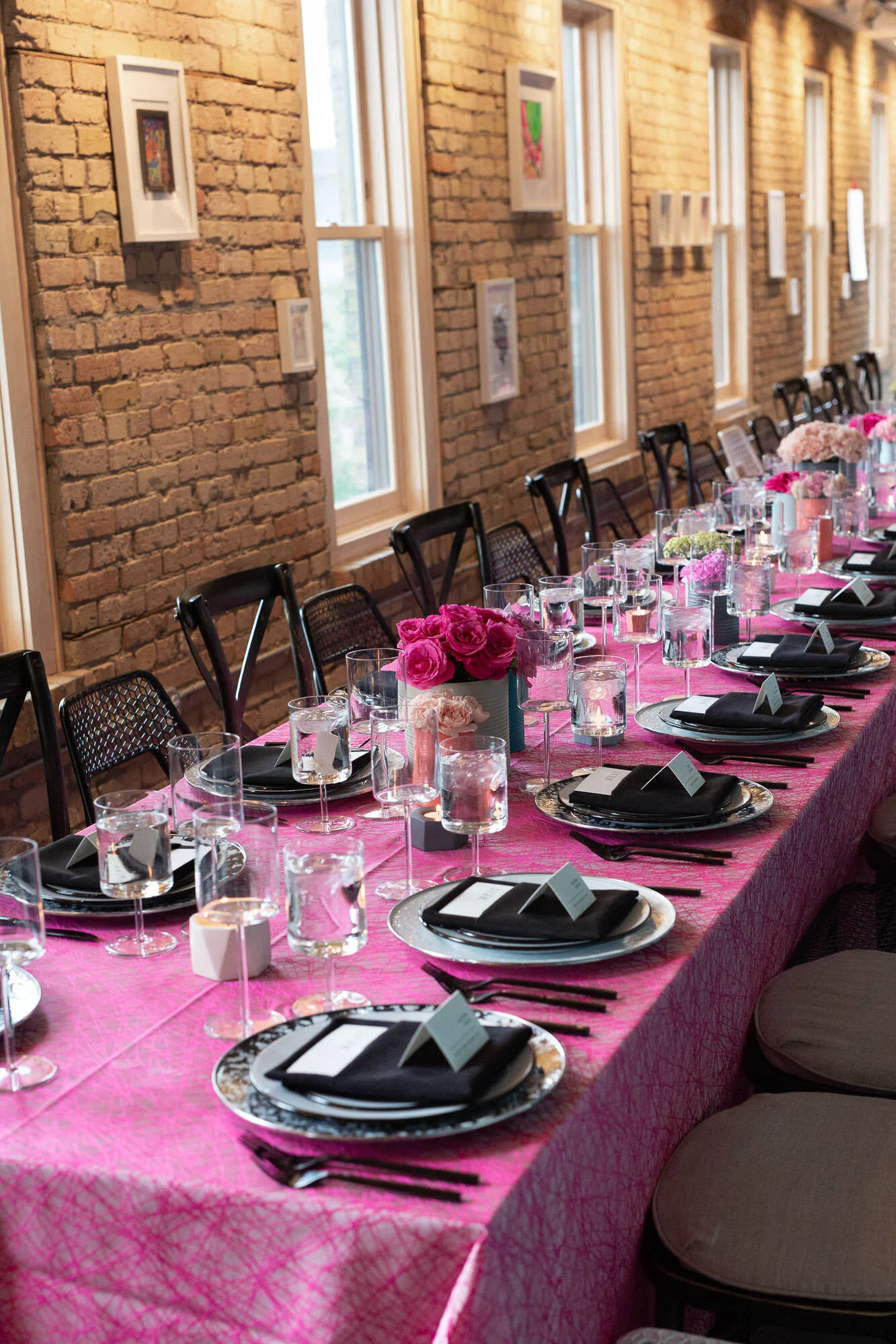  tablescape with pink tablecloth, painted tin can vases with bright floral displays, black silverware and black linens on plates 