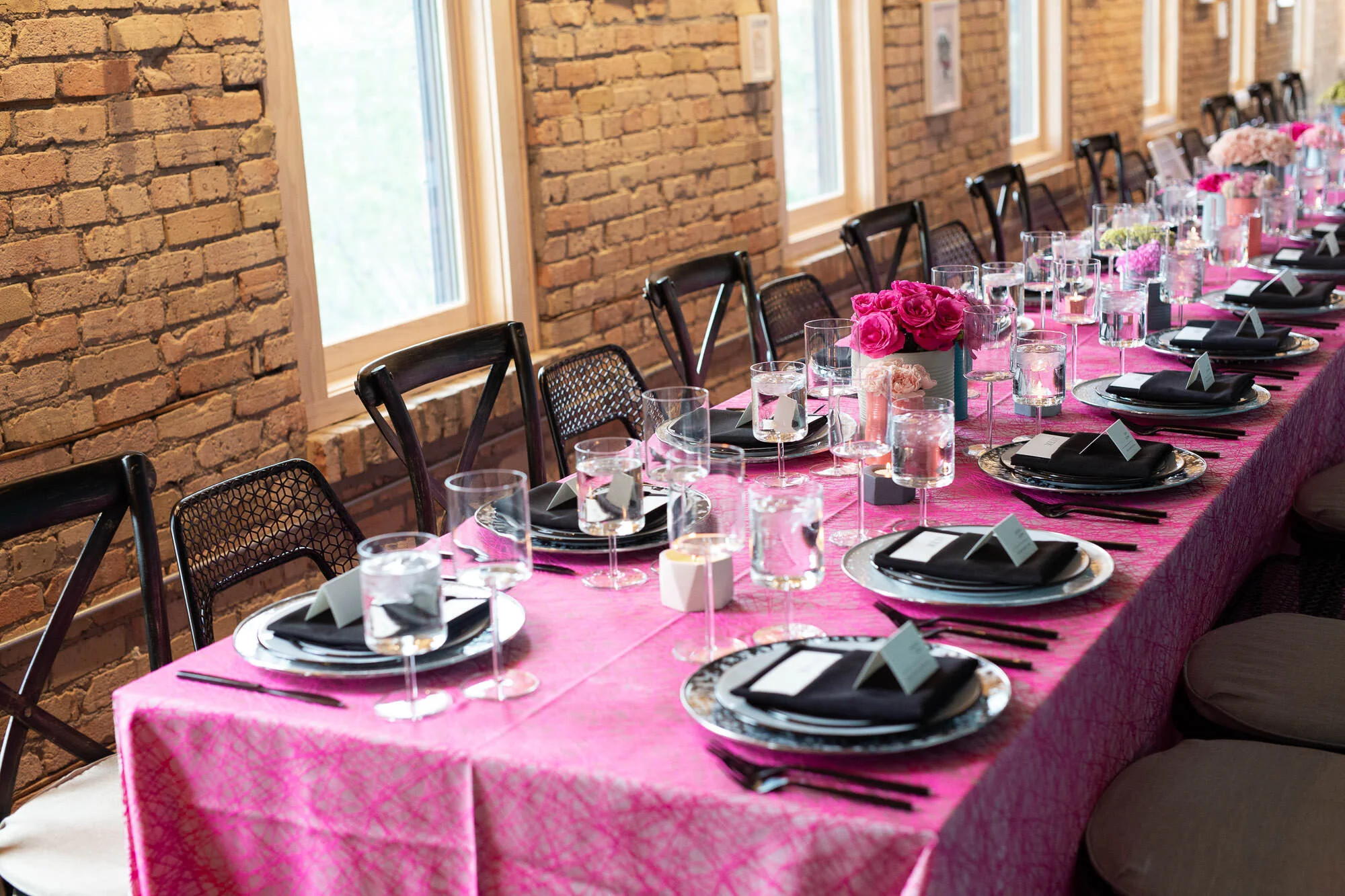  tablescape with pink tablecloth, painted tin can vases with bright floral displays, black silverware and black linens on plates 