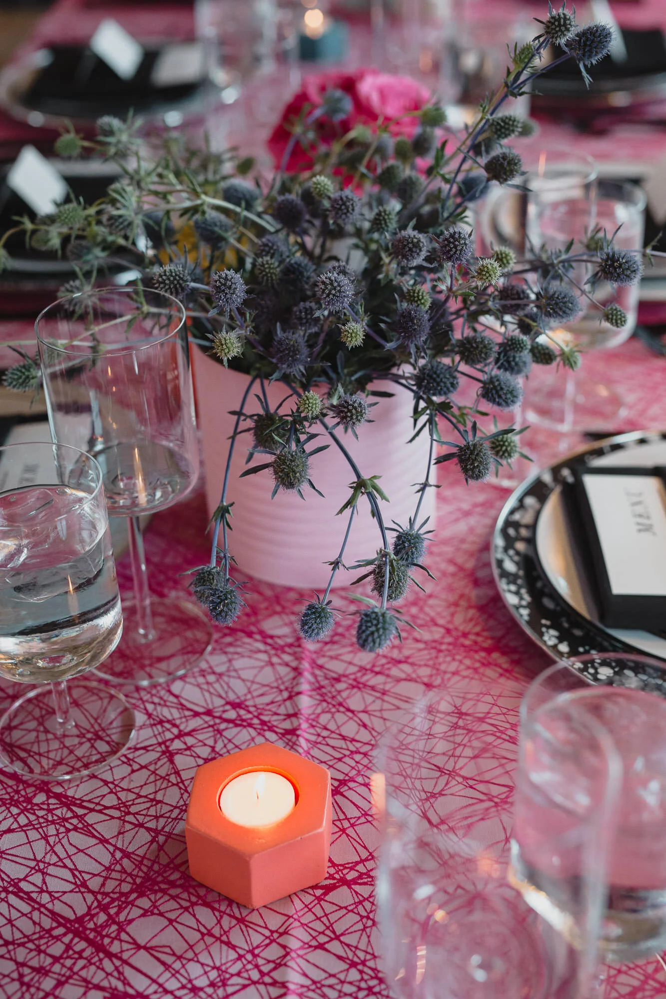  tablescape with pink tablecloth, painted tin can vases with bright floral displays, black silverware and black linens on plates 