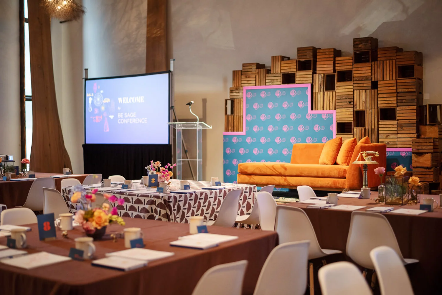  stage display with orange velvet settee, lucite podium, pink and blue floral backdrop, and wooden crates 
