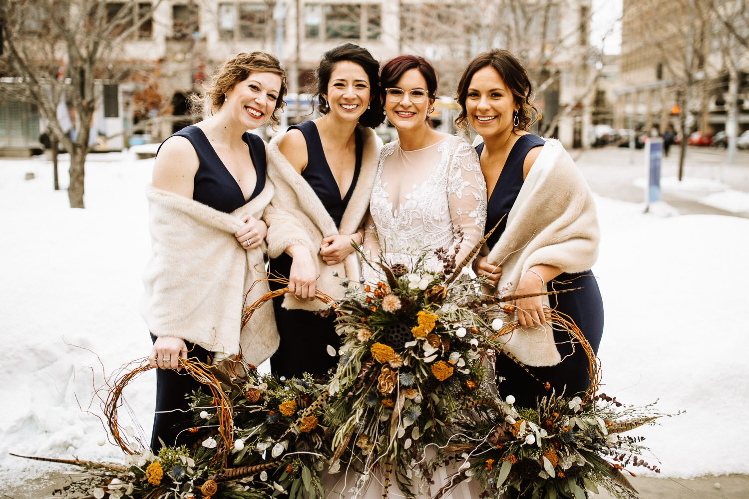 bride with bridesmaids wearing fur, camel stoles, and holding hoop bouquets of dried flowers and feathers