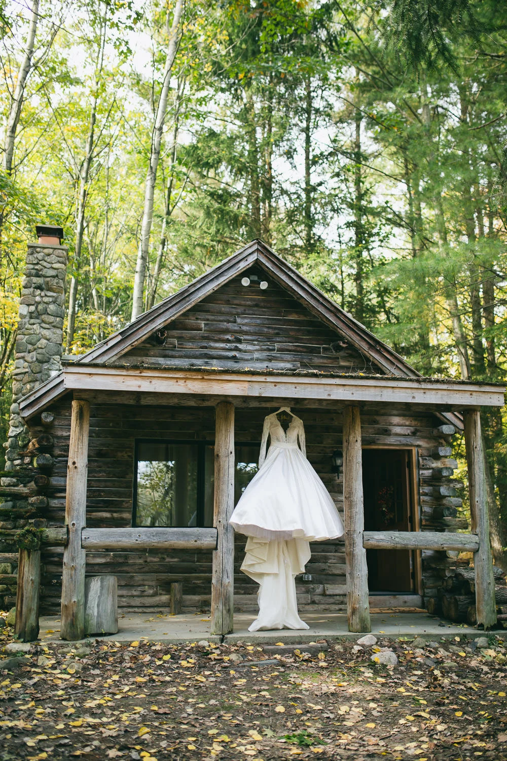  bridal gown hanging from rustic wood cabin with rock chimney 