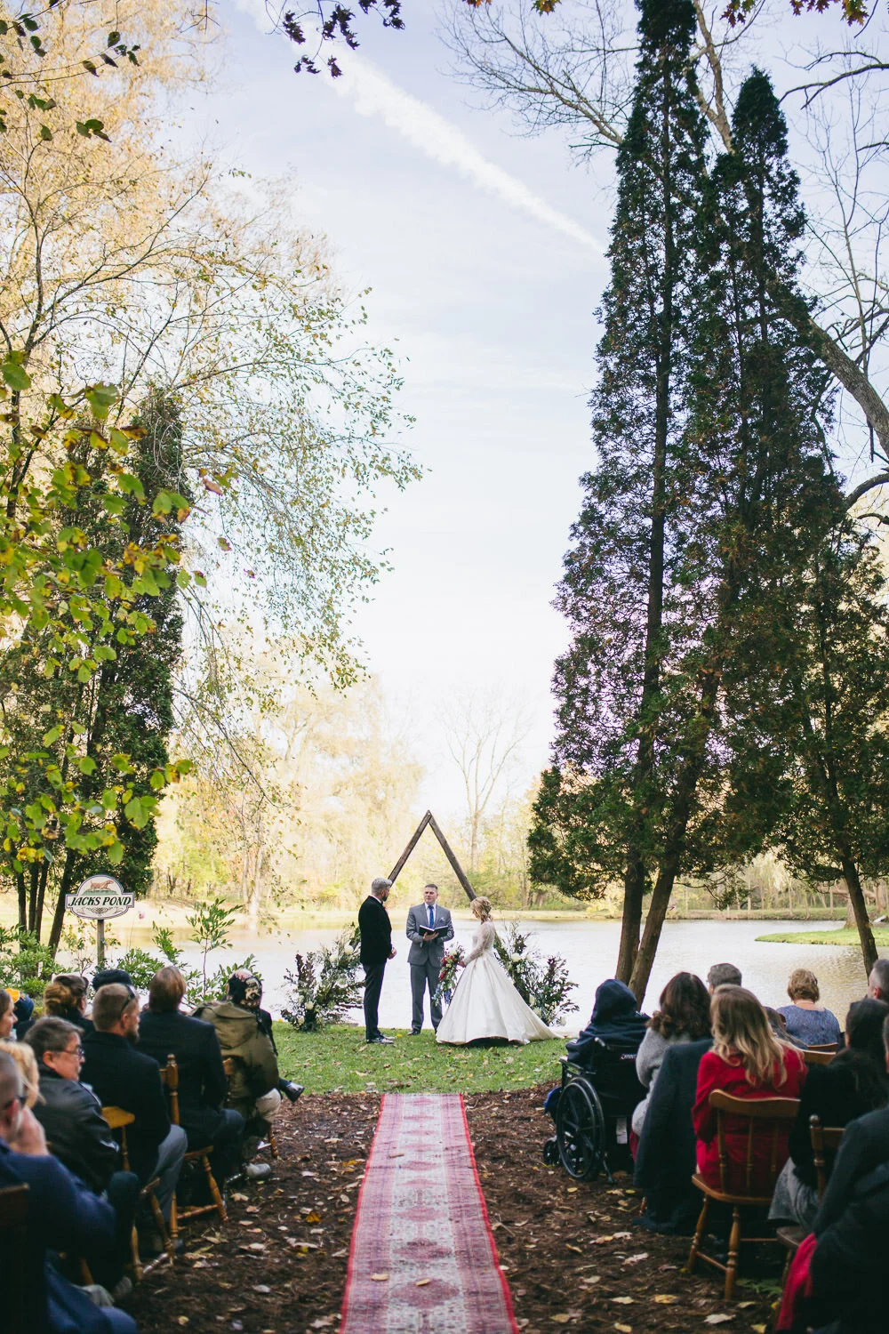  wedding ceremony by a pond with triangle altar and red rug runner down aisle 