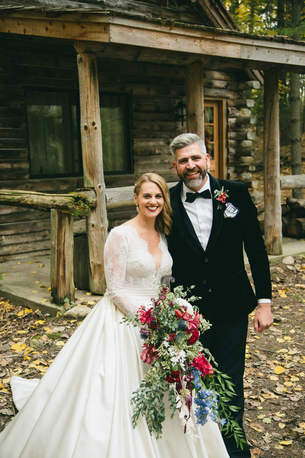  bride in long-sleeved lace dress and large rustic red white and blue bouquet and groom in black tuxedo 