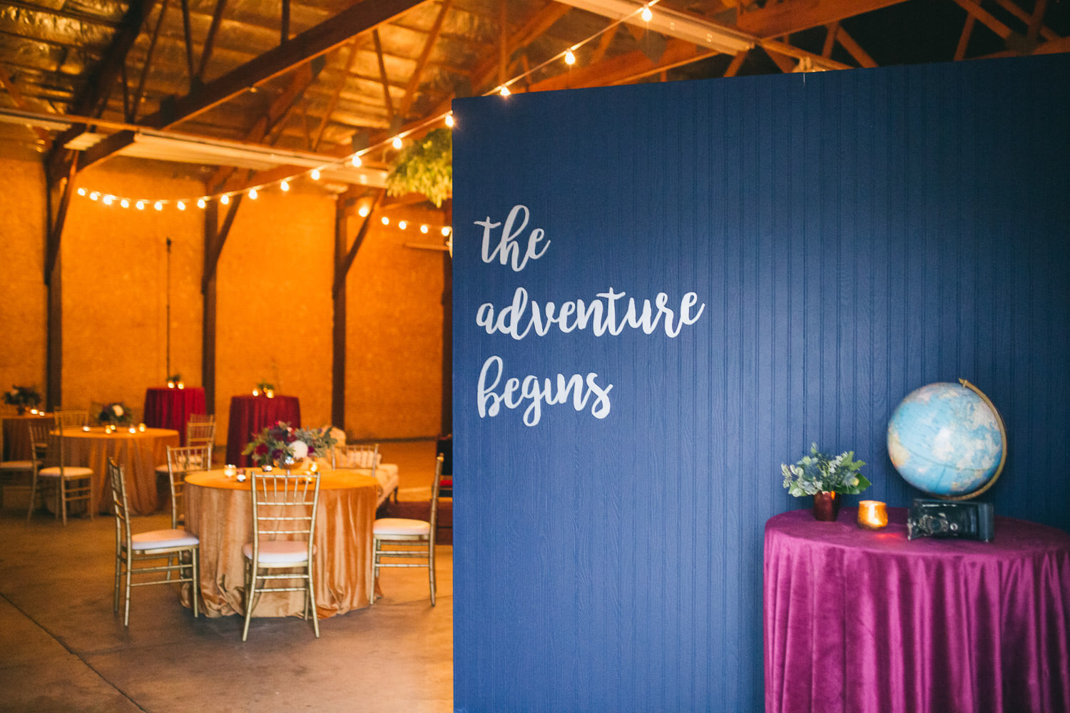  wedding reception in an airplane hangar with the words “the adventure begins” on the blue wall. 