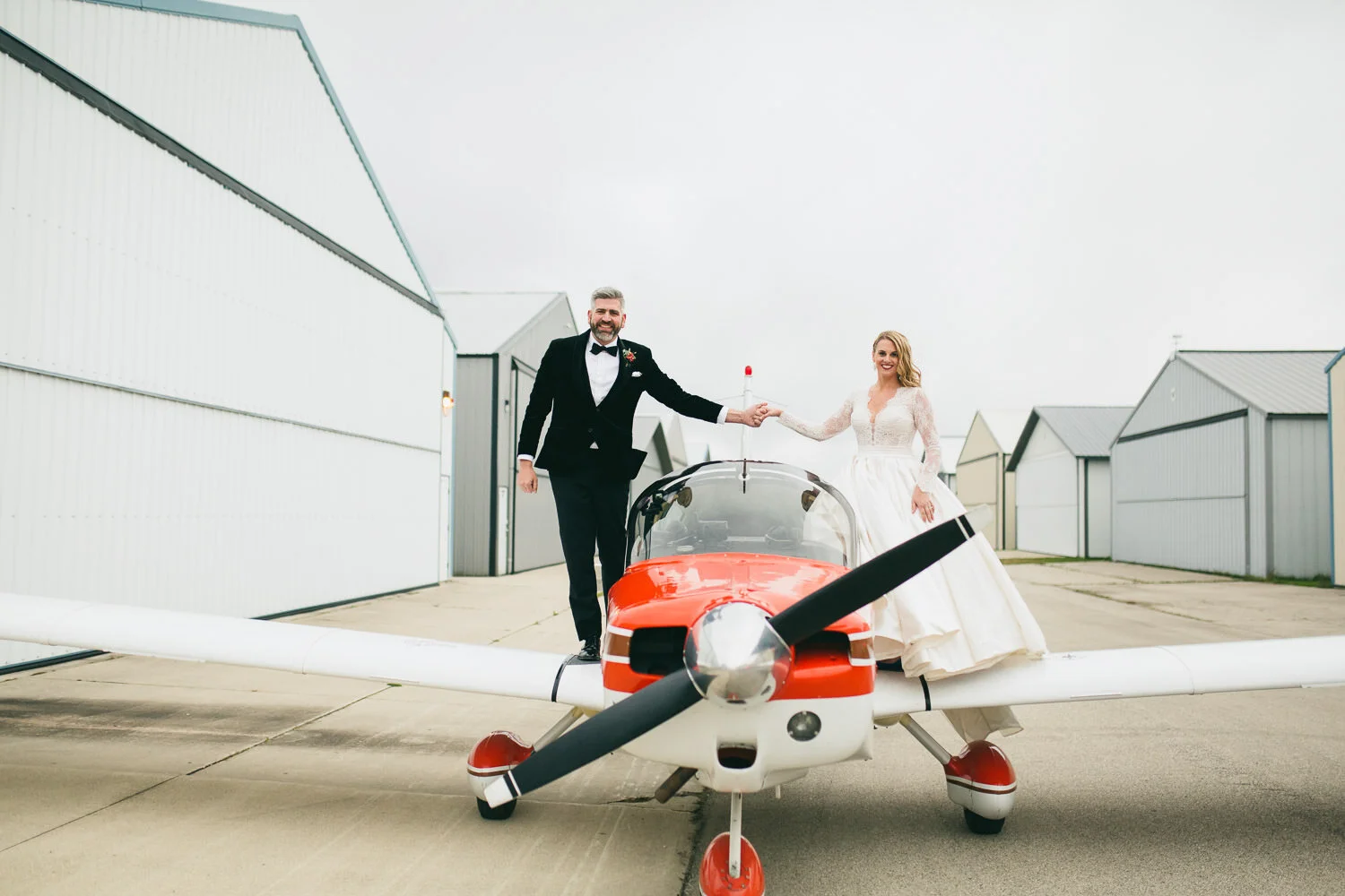  bride and groom holding hands and standing on wings of red and white airplane 