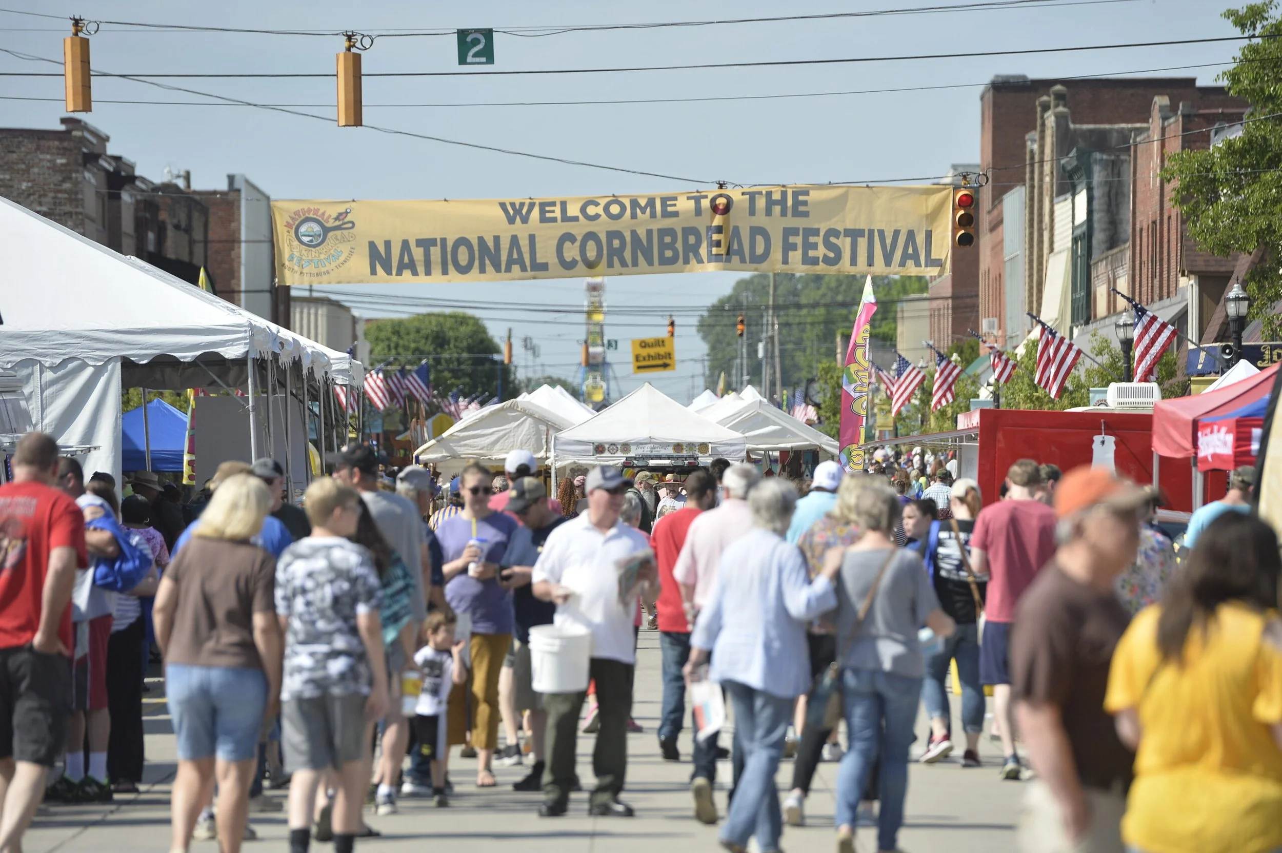 Banner that says welcome to the national cornbread festival with people walking around, filling the street