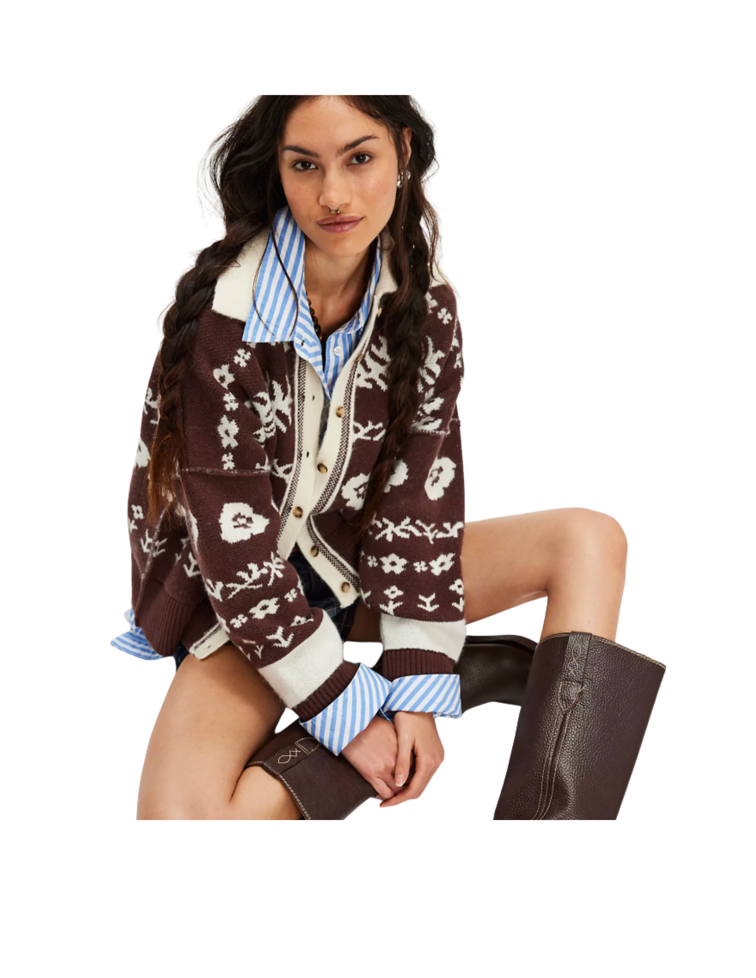 Young woman with long braided hair, wearing a November rain patterned sweater over a blue striped shirt, brown boots, and black shorts, sitting with one knee raised.