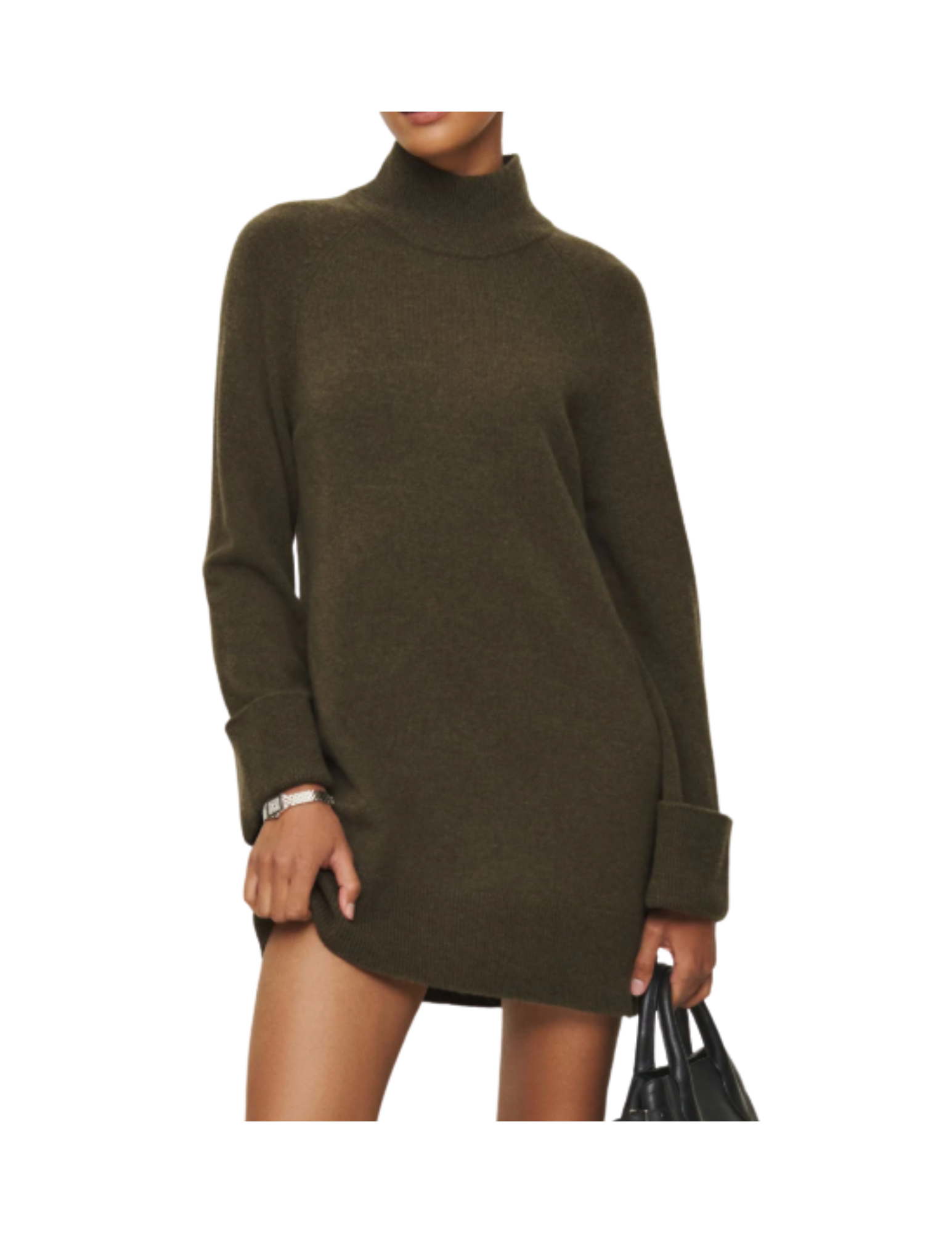 A woman wearing an oversized olive green sweater dress with a turtleneck, standing against a white background, holding a black handbag in her left hand.