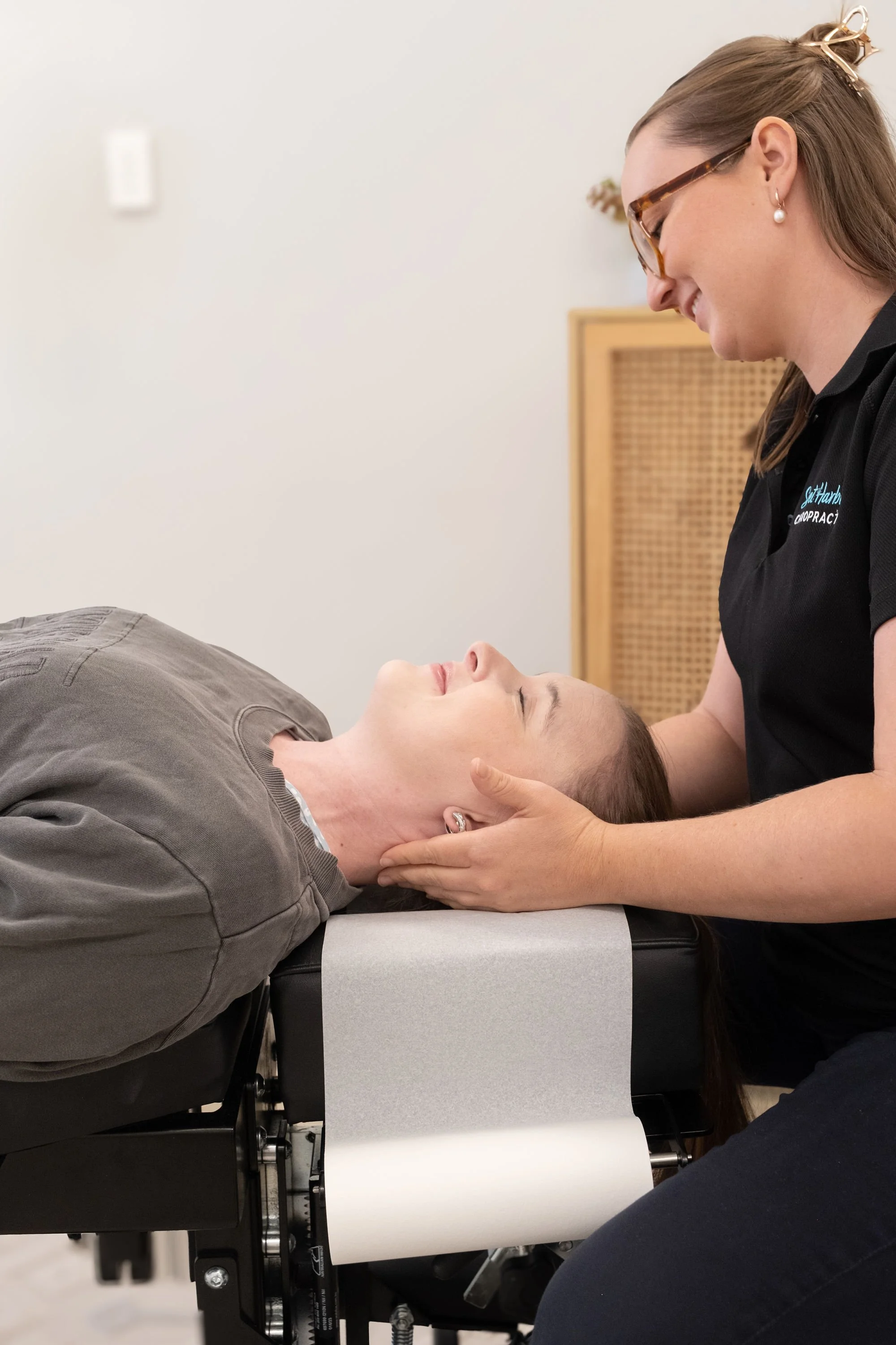 Client laying comfortably on table while Chiropractor gently checks neck both are smiling