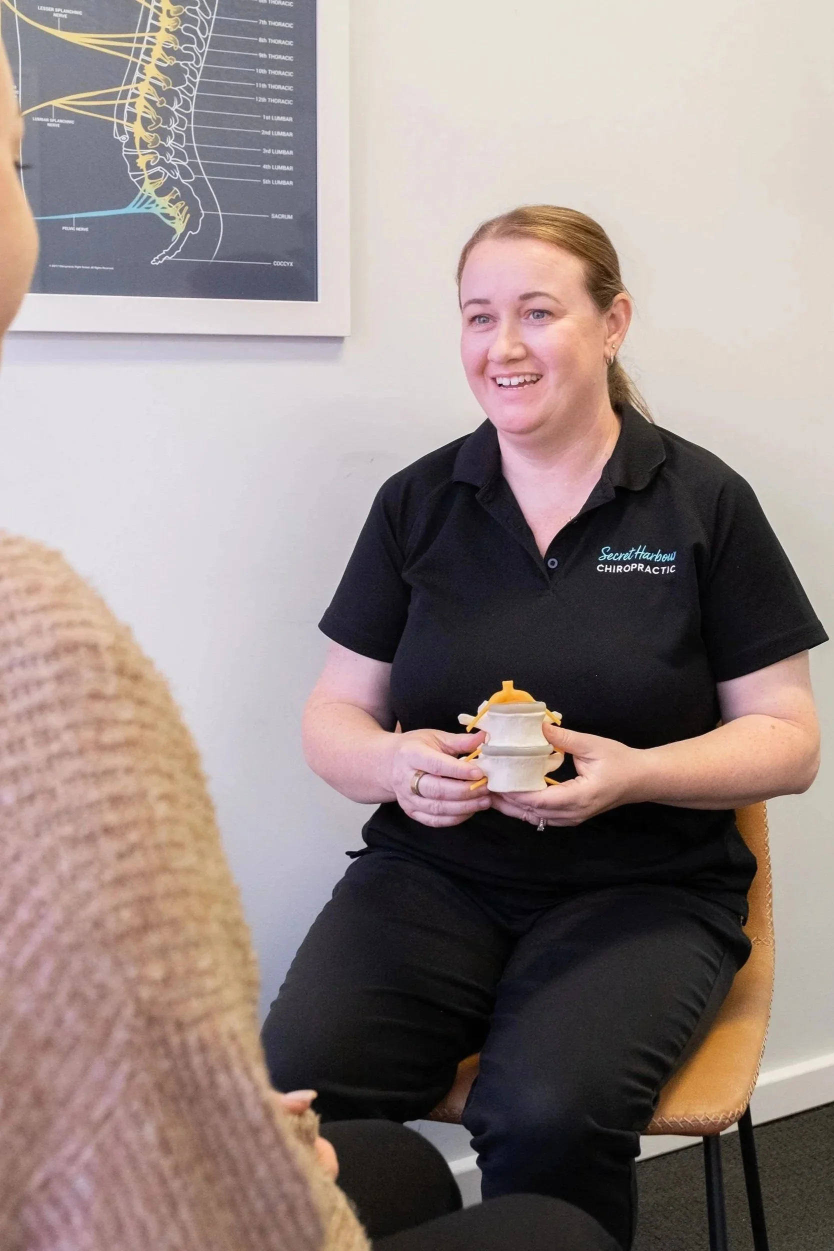 Chiropractor in professional clinical environment explaining spine model to client