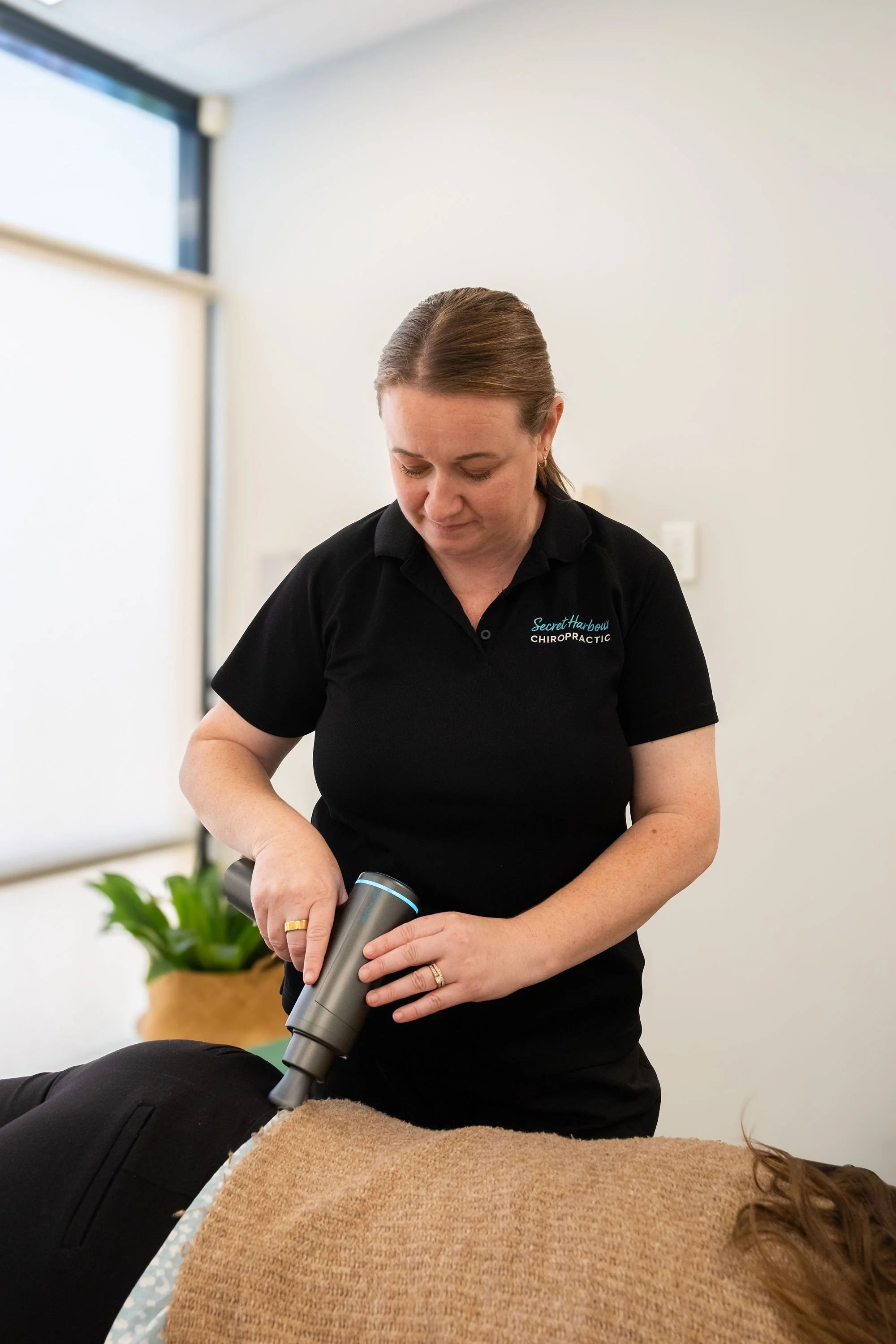 Chiropractor using massage gun to gently ease muscle tension