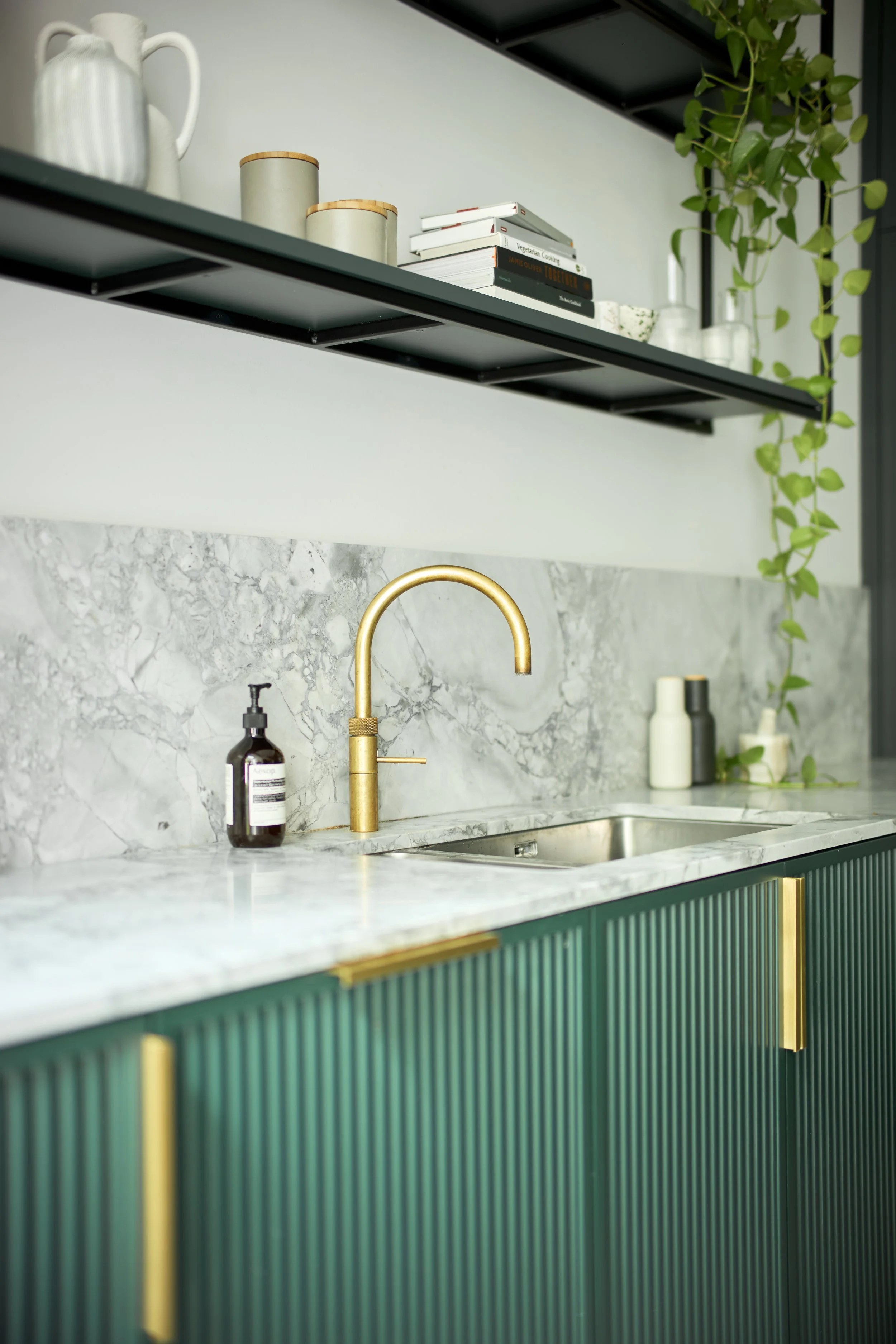 A close-up of the sink area of this bespoke kitchen, with fluted racing green doors, brass taps and handles, and emperador marble.