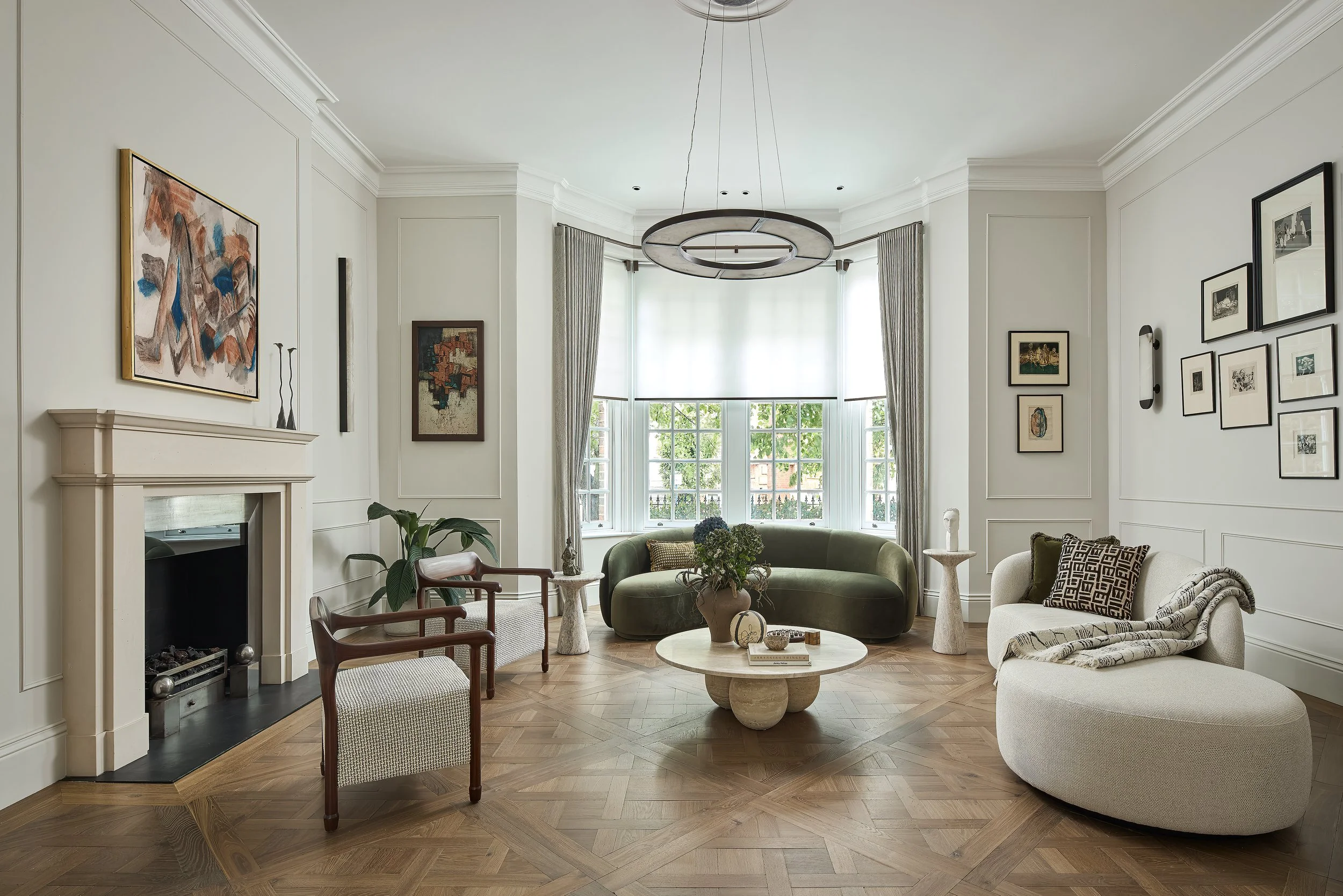A stunning reception room with versailles smoked oak flooring, alabaster lights, curved green velvet sofa, bespoke and sourced furniture and a collection of artwork belonging to our clients