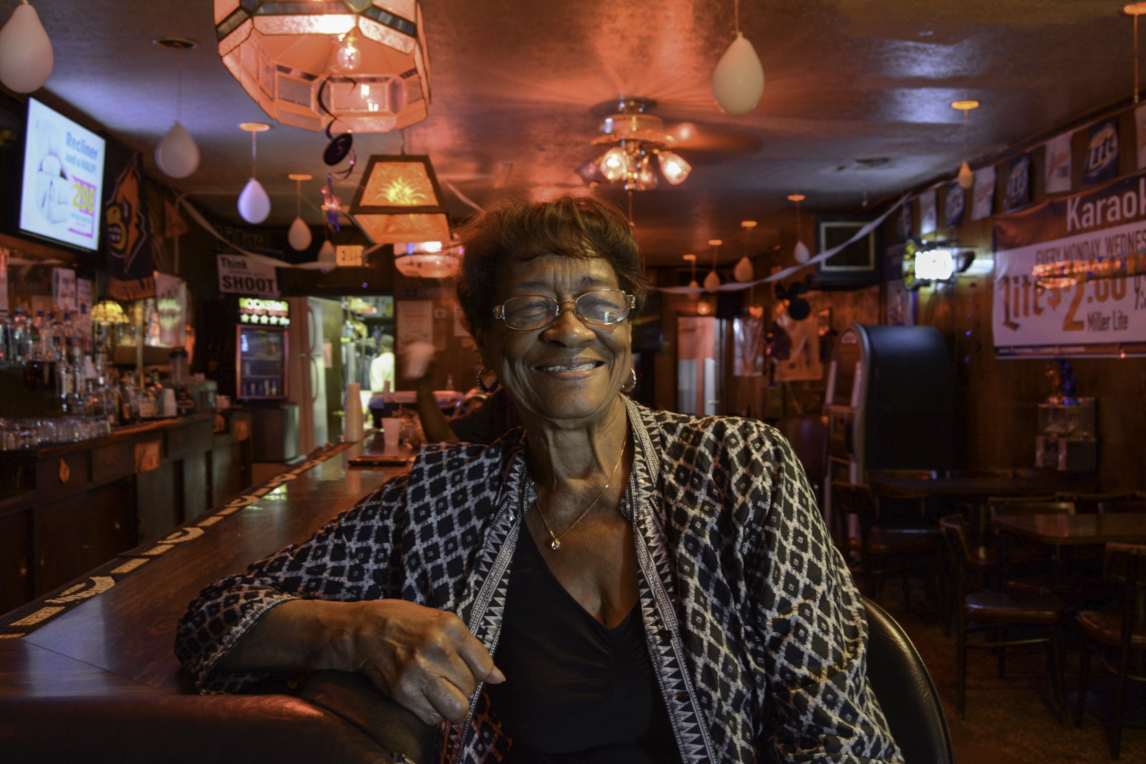 “Well, we will go back to the fifties, where it first started. This used to be a grill, it happened due to urban renewal. It came through and wiped out all the businesses. It wiped out all the black businesses on Muhammad Ali. The people that had the spot, made it a bakery. I think it was called Givens Catering and they were known for their pies and sweets and stuff like that. They had the business on Muhammad Ali, but when urban renewal came through, they moved over here. They built this little place and had a grill here instead of the bakery. So it was called Mills. Their last name was Mills, Homer and Juanita Mills, and they named it Mills Grill and it was a grill for quite awhile. Then Mr. Mills was stationed at Fort Knox. He was in the army and he had a lot of buddies that came in from Fort Knox and they were looking for a quaint little place to gather and have drinks and be in a safe environment. So he decided to change the grill to a lounge. So, it became Mills Lounge. He’d done very well with the Fort Knox crowd and then as time wound down and the guys began to leave the area, they lost a lot of the soldiers coming into Louisville. Then he and his wife decided that they were going to go their separate ways. So that was the end of the business. One wanted to keep this place and the other one wanted out and they could not afford to buy each other out. So, they came to the decision that they would sell the business and split it. My husband had retired from the Marine Corps. This was back in 1971 and he came back from Korea and got a job at Ford. He worked at Ford for twenty years. He was only thirty-seven when he retired from the Marine Corps because he went in when he was 17 and he had done 20 years, came out of the Marine Corps, got a job at Ford. I got a job at American Standard. That was a popular bathtub faucet and commode place that was on Seventh and Hill. So we landed good jobs and we'd done real well, you know, the pay was much better than being in the service. So, my husband did his 20 years at Ford and then he thought about retiring. He began to have a little heart problem and he thought, “I’d better come out, now, while I can enjoy myself.” So, he had a friend that was in real estate, Mr. Carl Hines, who was a very good realtor. He was talking to him, one day, talking about how he always wanted a quaint little bar or something. Carl looked at him and said, "I have just the place for you.", which was this place, here, and it was up for sale. So, the owners wanted a lot more than what we had, but the realtor said to make them a cash offer and that they just might take it because they're splitting up. They were gong their separate ways and they wanted out. So we made the offer and they took it. They were asking for $95,000, we offered them $50,000, they took it and walked out. They left everything just like it was. We used to have these little jukeboxes, along the bar, when I first came here. They were from the fifties. You'd put your quarters in and play music. When the computerized jukeboxes came along and all, there was no way to keep up with changing the records and everything. So, that was the end of that. They just became antiques and a guy came here one year, a white guy, on his way somewhere out west. He was going to open a diner and he wanted these little jukeboxes to be in the diner. He asked if I'd be interested in selling them and I told him that it depended on what he was going to give me. So, he made me an offer and I told him that he could take them the same day. So, we disassembled them off the bar, loaded him up, with his little trailer, and he was on his way. I wondered how it panned out, but I never heard anything from it. So, the bar deal went through but when I came up here, I looked at a business that really fell off and I could see why the old owner was getting out There wasn't a soul in here during the day. I told my husband that I didn't know about it. We were going to put every dime we got in this place and we didn't know if it would sink or swim. He really wanted to do it and we jumped right in. When my husband retired from Ford, he bought this. I came out of American Standard because they were scaling down. I came out in '88 and we bought this bar in '90. He ran it during the day and it really wasn't good, at first. We weren't making it. Then he had a lot of friends that were musicians, very good musicians, that had played with big bands all over and everything. But they really hadn't gotten their due. You know, they should have really made out and been big time, with big people, but they played around and then they came back to Louisville. One of his friends was in here, one day, an organ player. He just died about three or four months ago, his name was Billy Madison and he was phenomenal and he wanted to know if he could play organ in here. He'd get a couple of guys with him. He had a drummer and a saxophone player and they came and set up right in that corner, over there. It would be crowded when they played. The original owners had been closed on Thursdays, so Thursday was our worst day. People were not coming on Thursday so we didn't do anything. So we're like, you know, let's try the band on Thursday and see if that'll loose things up. A lot of naysayers said we would never make it. Well, we tried it and it took off. Thursday was our best night. It would be running over. Thursday was so good that we decided to go to Friday and then Saturday. So after awhile Thursday, Friday and Saturday we had jazz here. We never charged a cover charge because the same people came all the time. They were regulars and they didn't feel comfortable paying to come in to spend. They felt that if they would come here, they were going to help pay utilities and everything. A cover charge would have helped because it always helps you to fray the costs of the band. You gotta sell a lot of lot of drinks to pay your band and your waitress and your bar maid and everything and then make something, you know. But they made it work and I had some regulars that came. I called them my utility people because they kept the lights on and stuff on all the time. In 1994, my husband began to have a problem with his heart. They diagnosed him as a diabetic. He never had a problem with his health. He had diabetes and a heart problem. He had a slow heart beat and unbeknownst to me, his doctor told him it was cardiomyopathy, which is irreversible heart failure. He knew this and did not tell me this. So from '90 to '95, he worked the bar and then he'd begin to slow down and get kind of sick. I was here one night, I went home, he said he didn't feel good so he didn't come to the bar and I went home and I have fixed dinner and everything and he didn't eat. I said, "Well, what was wrong with the food? You didn't like it?". I didn't get a response, and then I heard a weird noise. Have you ever heard a person die and they make a loud, like a gurgling sound? And I went in there and I thought, “What in the world is that?”. I looked and he was laid back and had this gazed look. I shook him and there was no response, so I called 911. It didn’t take them long to get there. They came in full force and they tried everything. They tried the electric shock and everything. They said, "Well this is not working and we're gonna take him onto the hospital." They went to Jewish. I called my son and he met me at the hospital. Thank goodness my son was there with me. They told me that as soon as they got him stable, they’ll let us go back there. We sat in that waiting room for an hour, just waiting. After a while, I'd told my son that something was wrong. It was taking them too long. So we went up to desk and the guy told us that the chaplain was getting ready to come out and talk to us because my husband didn't make it. It was a low blow. You know how a balloon loses its air after it’s been popped? That’s how I felt. He was gone. My husband told me that if anything happened to him, to get rid of this place. Everything was going so well and I didn’t have anything else to do and I was in love with this place. So I was like, let’s try to keep it going. So for almost two years I ran this place by myself. I'd come in at 2:00 in the afternoon to 2:00 in the morning. I had a girl that helped me during the day and then I was here. I didn't have anything else to do, you know, and it helped me get through it. I was married for like 42 years to my husband. And then for him to go like that was just something that I didn’t plan but we survived it. So from like ’95 up until now, I've been in here every night and I think it helps keep me young.” - Ms. Syl, owner of Syl’s Lounge in Russell