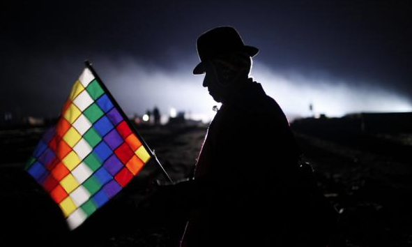 An Aymara man holding a Wiphala flag representing the people of the Andes