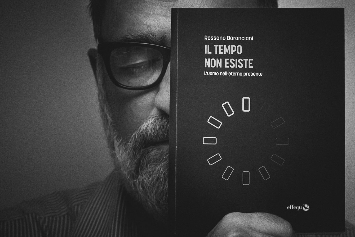 Foto bianco e nero in studio di Marco Arienti che si copre parte del viso con il libro 'Il Tempo Non Esiste' scritto da Rossano Baronciani.